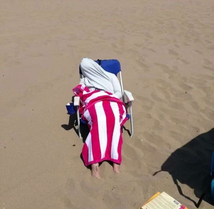 женщина лежит на пляже обмтонанная одеялом